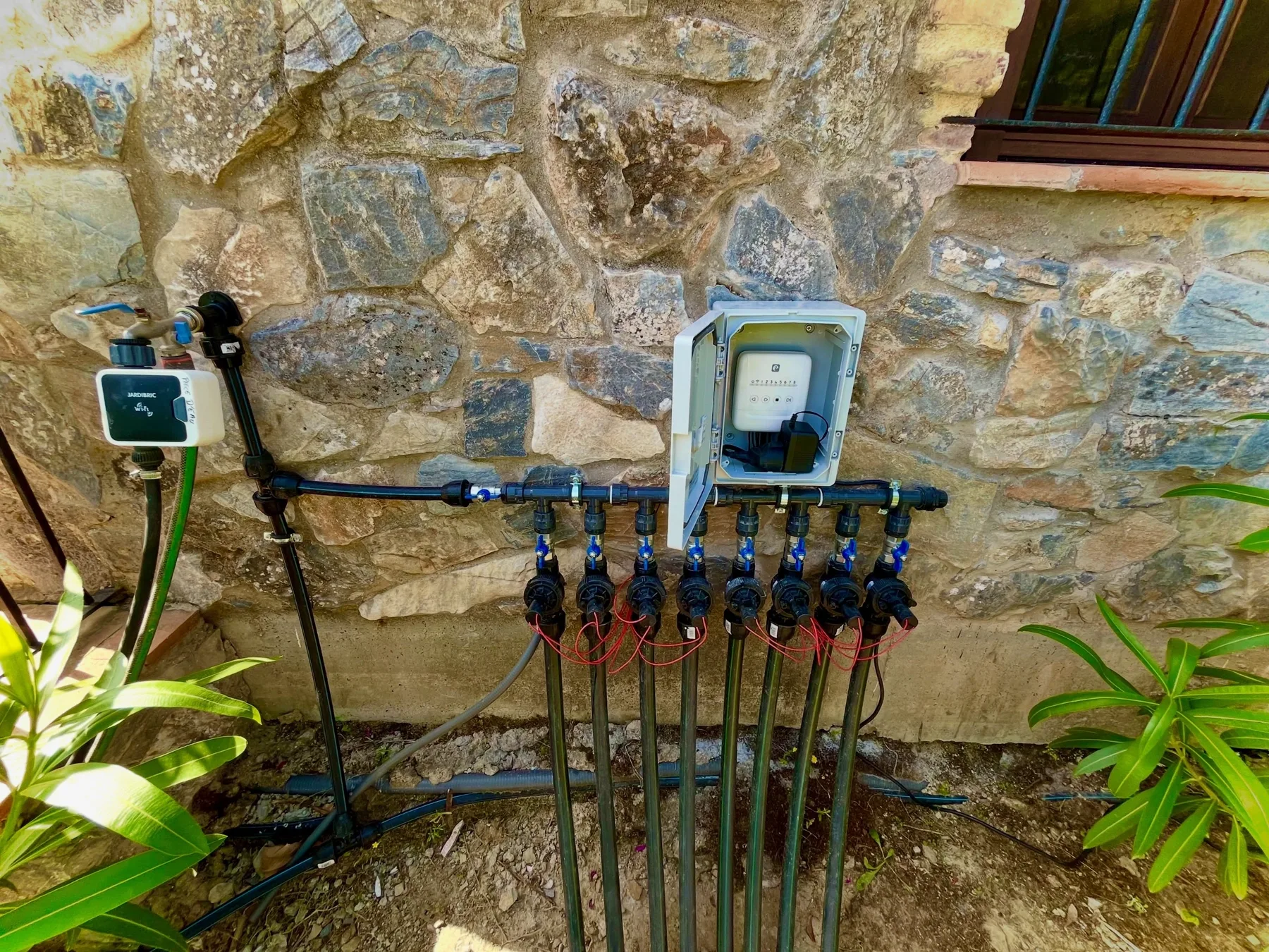 Programador WiFi de riego y colector de electroválvulas instalado en muro de piedra